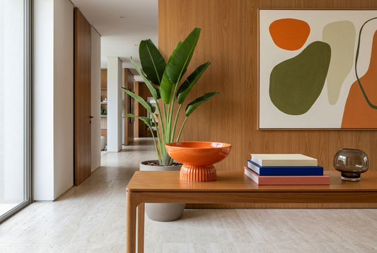 Bowl naranja en una ambientación contemporánea con libros de color y planta tropical