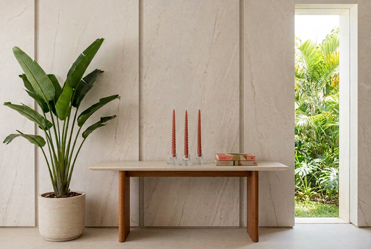Tres velas Twister Terra en portavelas de vidrio sobre arrimo contemporáneo con fondo de piedra, libros y planta tropical.