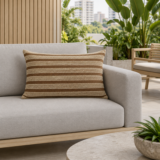 Cojín rectangular caramelo con franjas crema en relieve sobre sofá gris piedra en terraza contemporánea