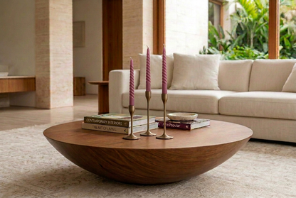 Velas Twister en tono morado ciruela sobre portavelas de bronce, en living con mesa de nogal y alfombra clara.
